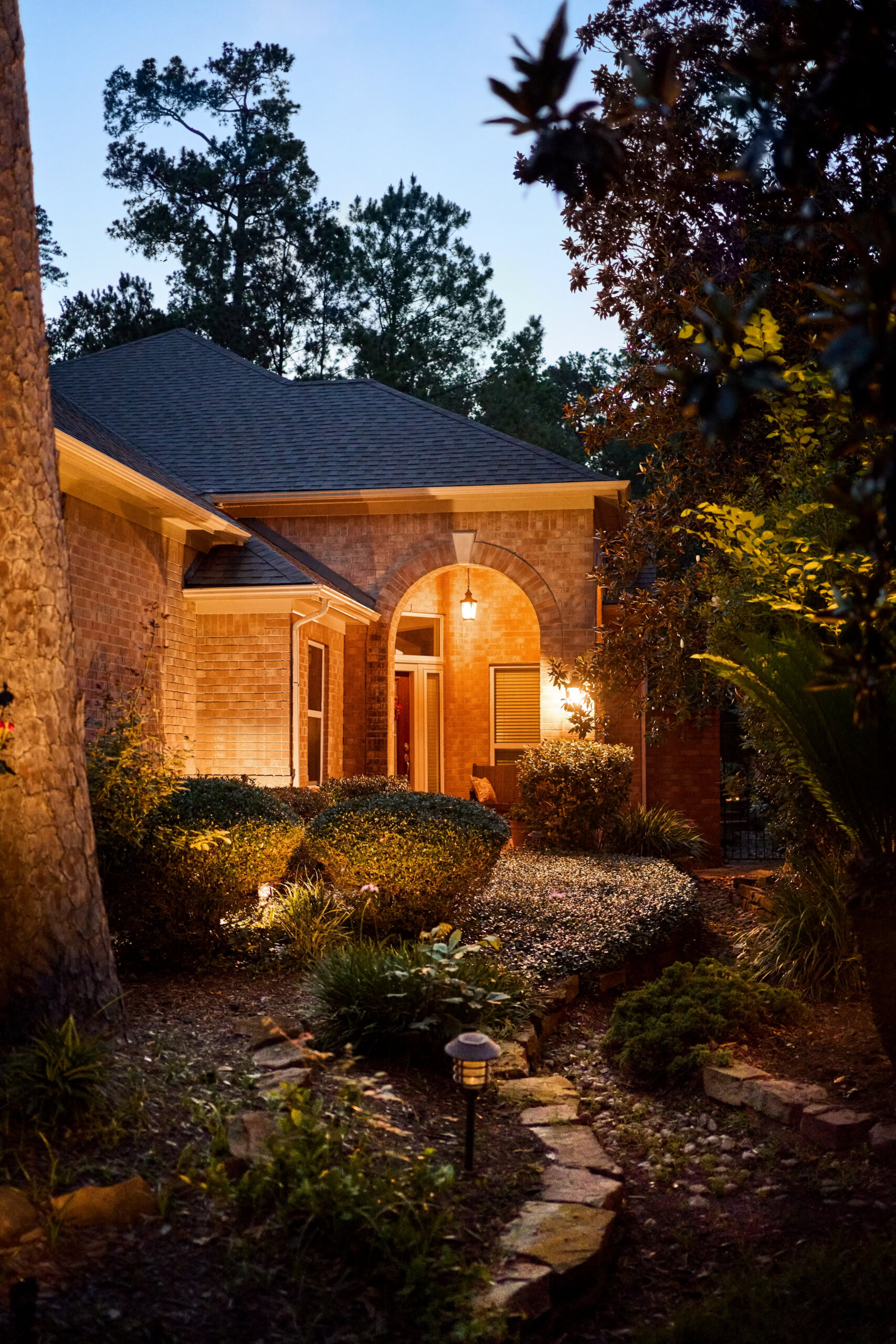 Exterior view of stone and brick home with lush greenery at night - Nighttime version